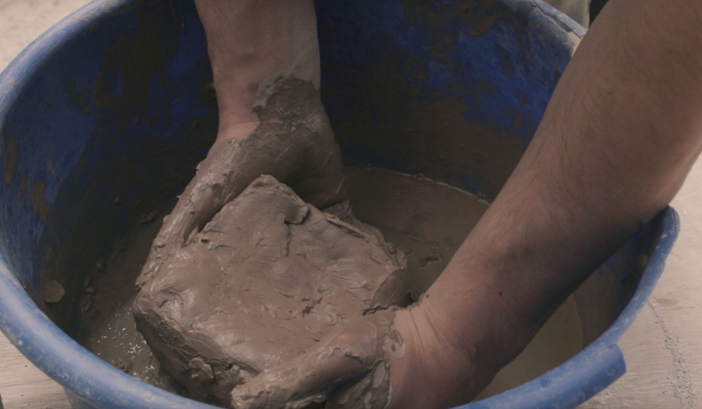 Hands mixing clay in a blue basin.